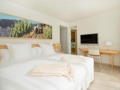 Helles Hotelzimmer mit Doppelbett, Schreibtisch und TV, schlicht und modern eingerichtet.