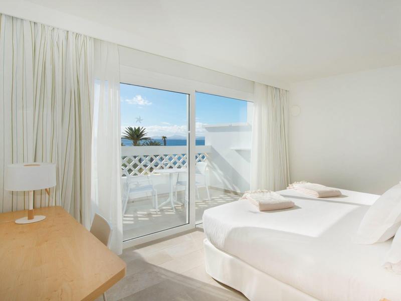 Chambre lumineuse avec lit double, bureau et vue sur la terrasse et la mer.