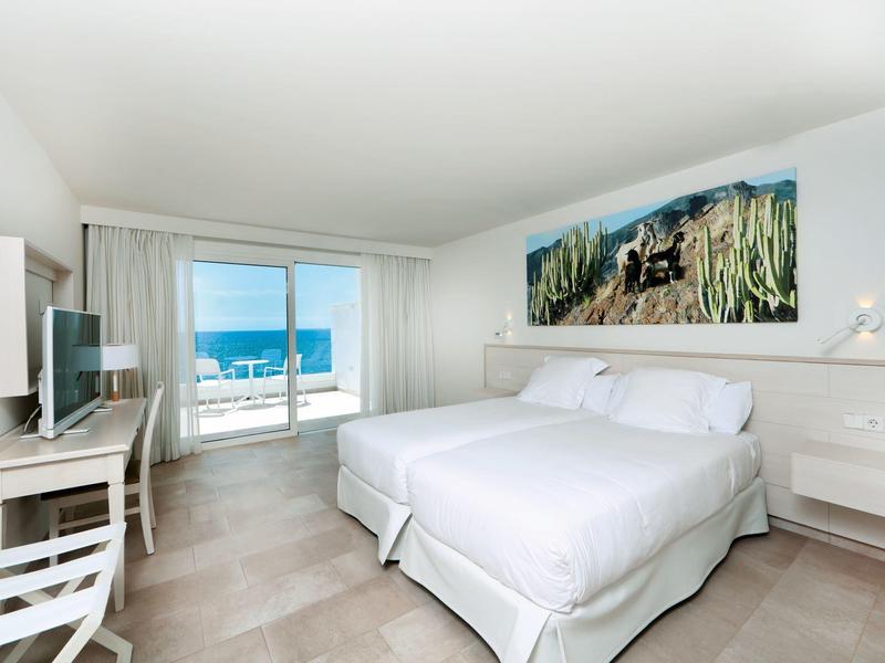 Chambre d'hôtel moderne avec lit double, vue sur la mer et design lumineux et minimaliste.