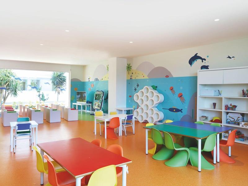 Salle de jeux colorée pour enfants avec tables, chaises et décoration murale d'animaux marins.