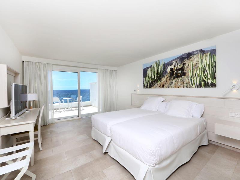 Chambre d'hôtel lumineuse avec deux lits blancs et balcon offrant vue sur la mer.