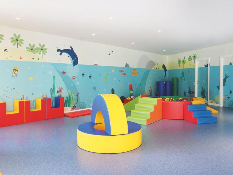 Aire de jeux intérieure colorée avec structures d'escalade, toboggans et balançoires dans une pièce lumineuse.