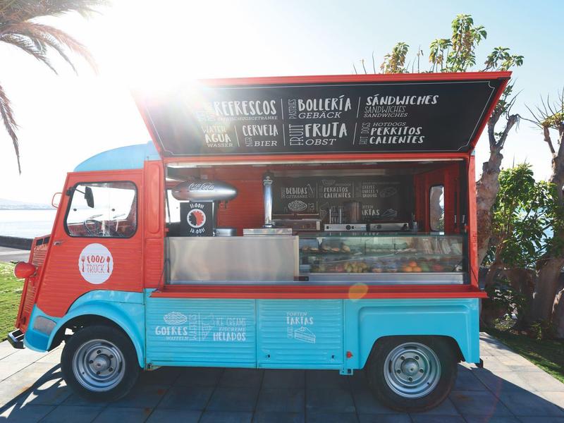Camion-restaurant coloré sur chemin pavé avec fenêtre ouverte sous le soleil.