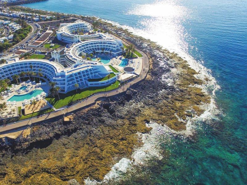 Complexe hôtelier avec piscines rondes et accès à la mer sur une côte rocheuse.