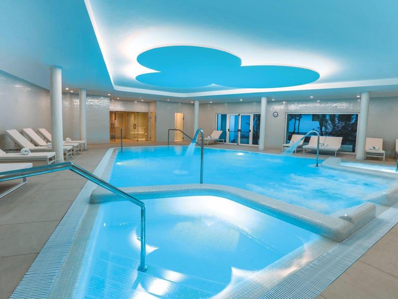 Piscine intérieure avec éclairage bleu et chaises longues modernes autour.