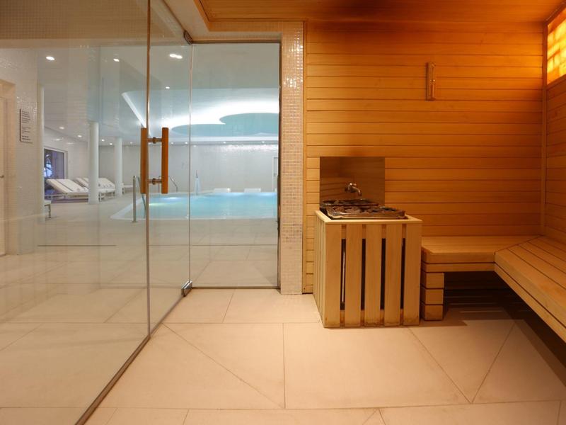 Espace bien-être moderne avec sauna en bois et piscine intérieure derrière une porte vitrée.