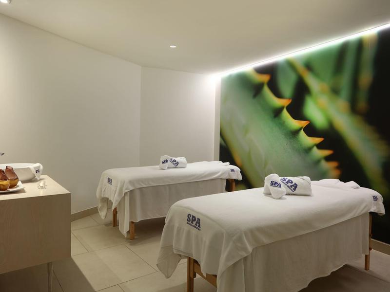 Deux tables de massage avec draps blancs dans une salle spa calme avec une image naturelle verte.