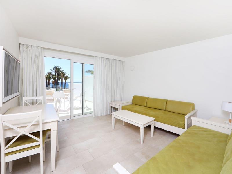 Salon lumineux avec canapés verts, mobilier blanc et vue sur terrasse et mer.