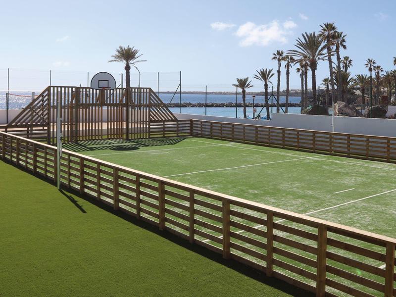Terrain de sport en plein air avec gazon synthétique et vue sur la plage par ciel dégagé.