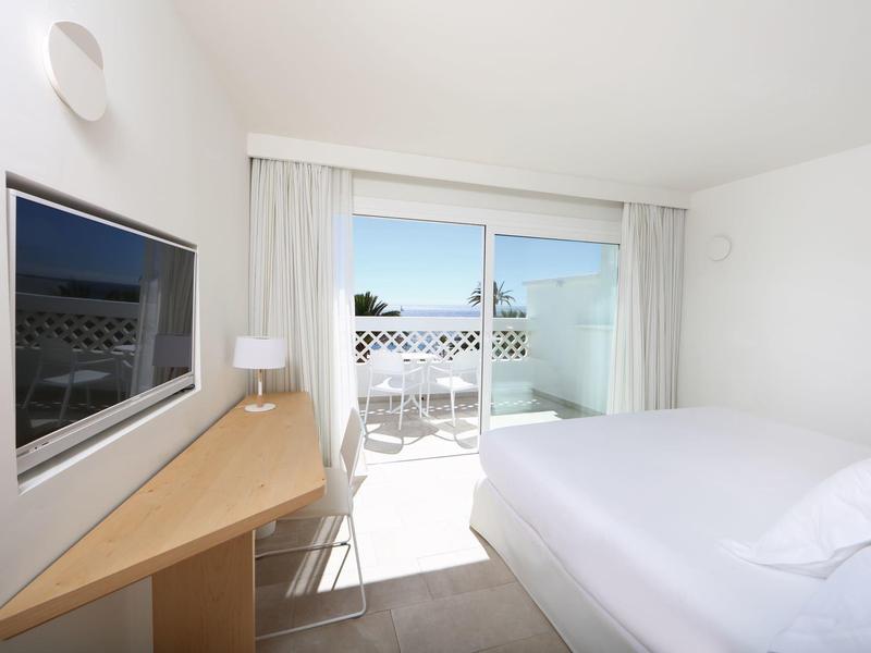 Chambre d'hôtel lumineuse avec lit double, TV, bureau et accès au balcon avec vue sur la mer.