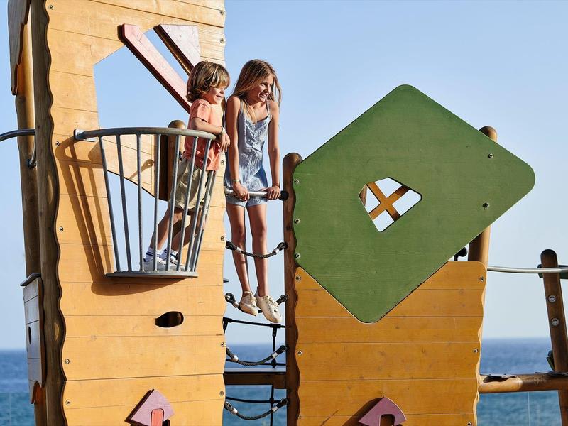 Des enfants jouent sur une structure d'escalade colorée avec la mer en arrière-plan.