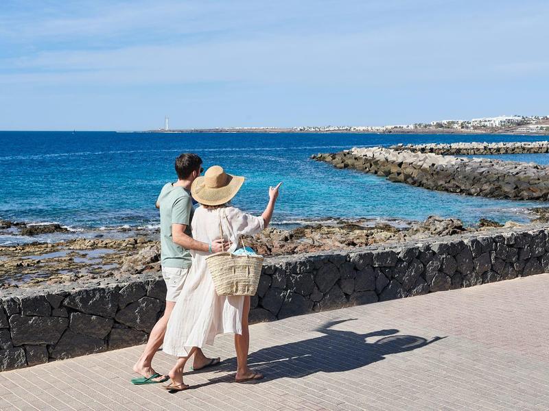 Un couple se promène au bord de la mer, regardant l'eau bleue et la côte rocheuse.