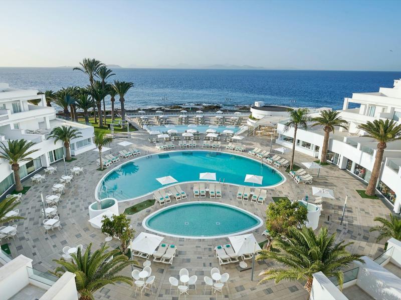 Piscine d'hôtel moderne avec deux bassins, chaises longues et vue sur la mer.