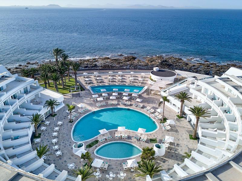 Hôtel moderne avec deux piscines rondes, transats et vue sur la mer et la côte rocheuse