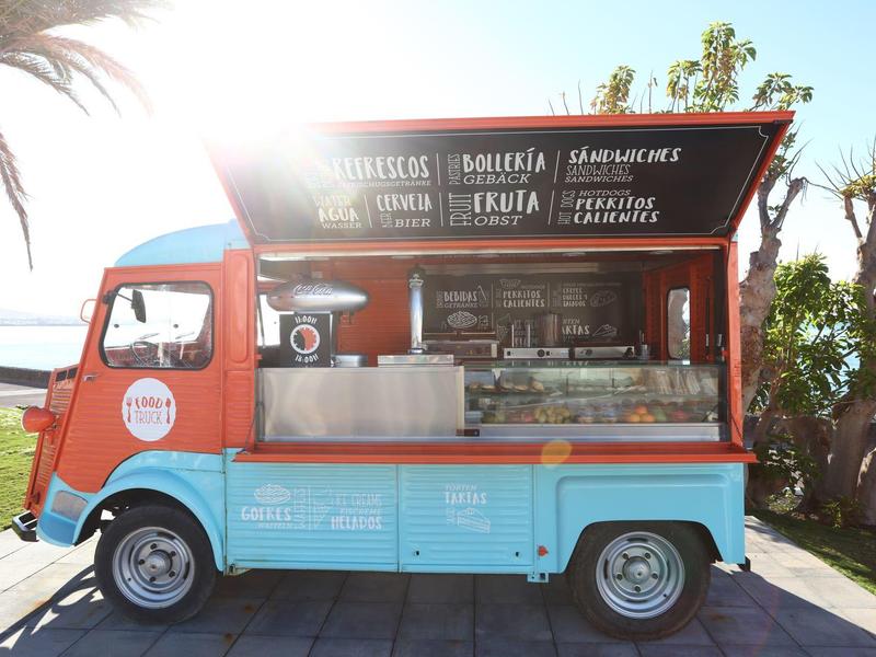 Camion-restaurant mobile proposant glaces et boissons près de palmiers ensoleillés.
