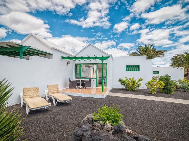 Cortile di una moderna casa per vacanze bianca con lettini e piante sotto un cielo blu.