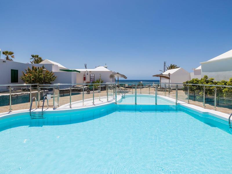 Piscina con acqua limpida davanti a bungalow bianchi e cielo blu vicino al mare.
