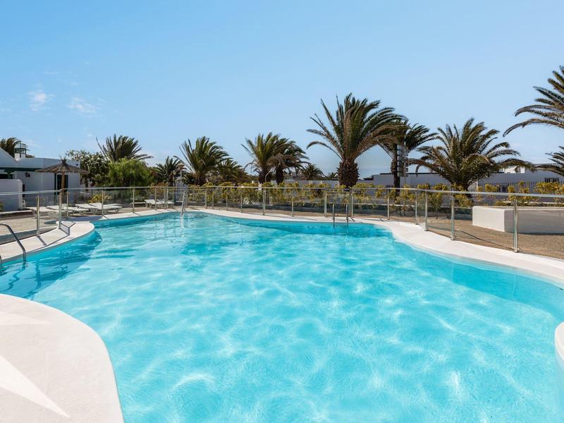 Piscina all'aperto con acqua limpida, circondata da palme e terrazza soleggiata.