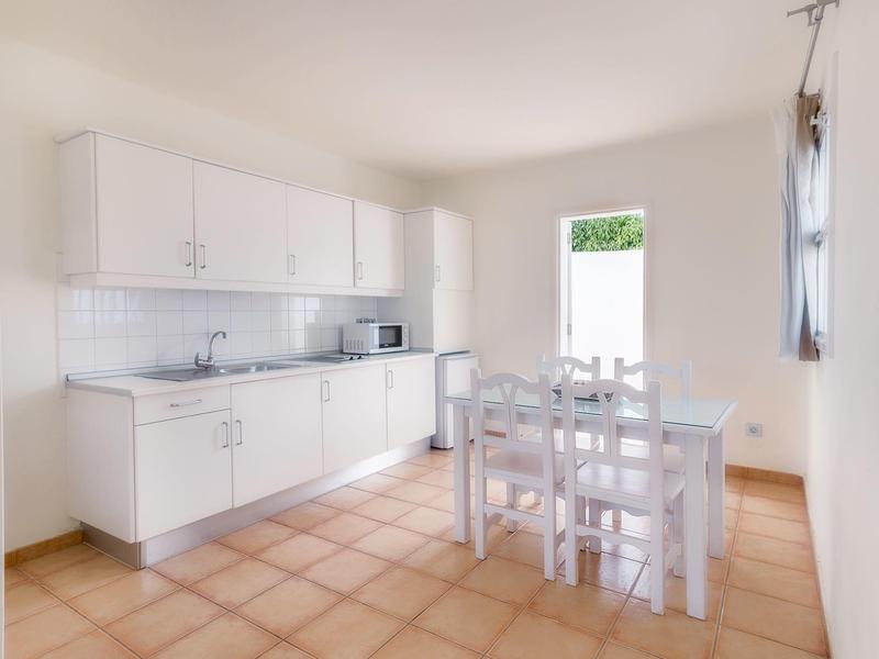 Cucina luminosa con armadi bianchi, tavolo da pranzo e grandi finestre in una camera d'hotel.