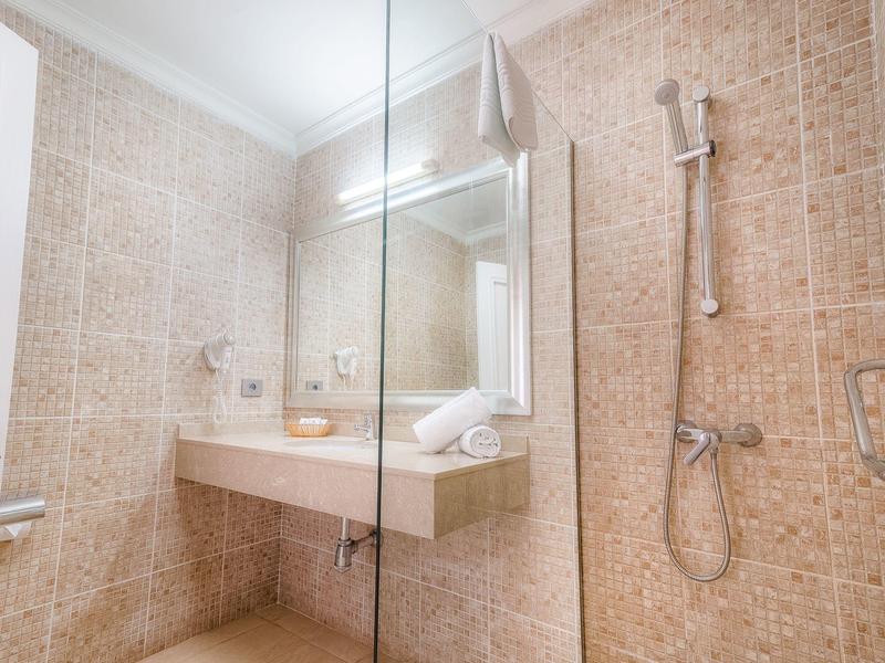 Bagno luminoso con pavimento e pareti piastrellate beige, lavandino incorporato e specchio con illuminazione.