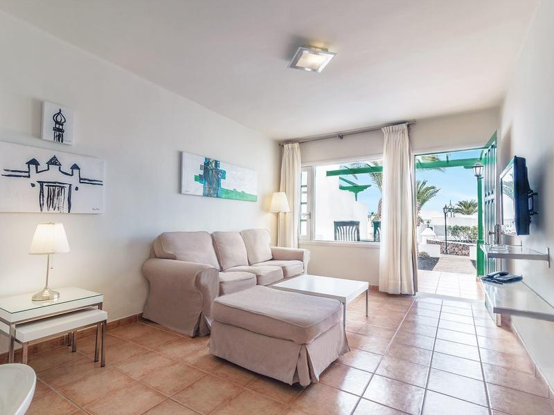 Soggiorno luminoso con divano beige davanti a grandi finestre e accesso alla terrazza.