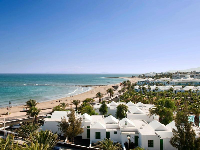Vista su edifici bianchi e palme lungo la spiaggia con cielo azzurro e mare