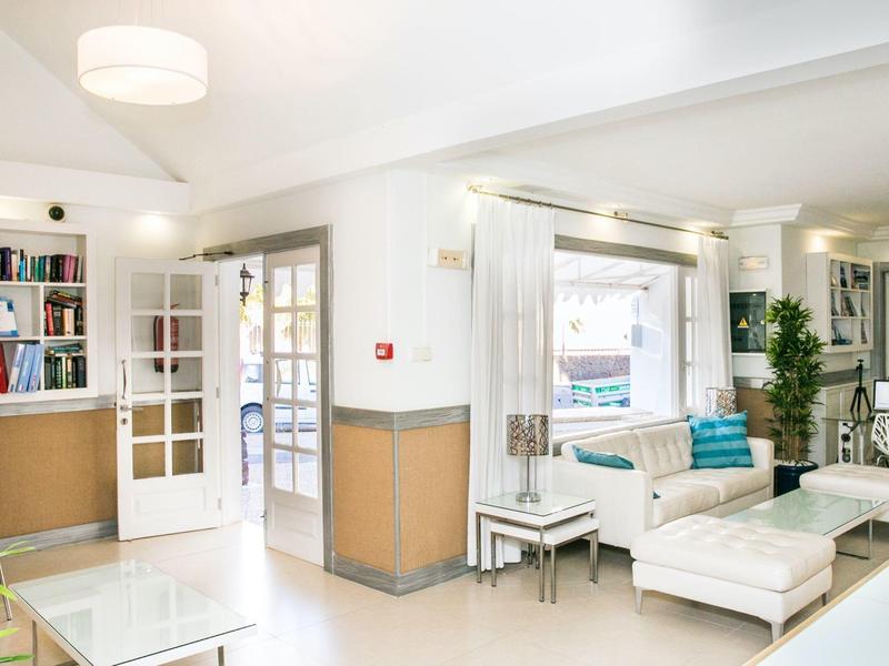 Soggiorno luminoso e moderno con mobili bianchi e libreria in un hotel.