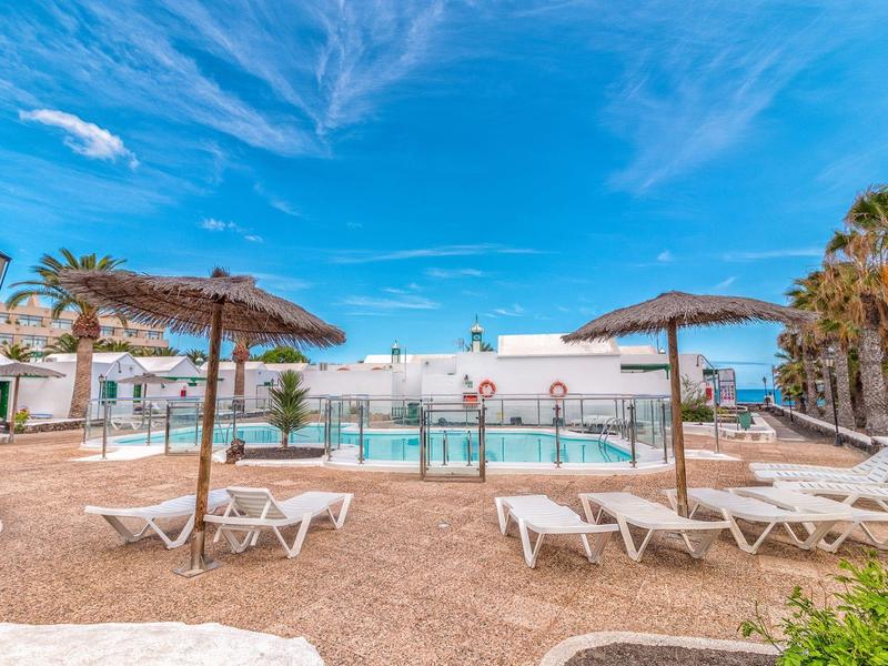 Piscina dell'hotel con lettini e ombrelloni di paglia sotto un cielo azzurro.