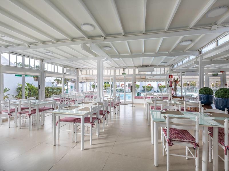 Ampia e luminosa sala da pranzo con tavoli bianchi e cuscini rossi in un hotel.