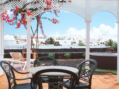 Terasa se skleněným stolem, židlemi a kvetoucím stromem pod bílým baldachýnem.