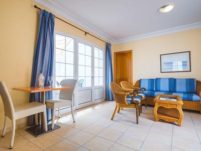 Jasny salon z wygodnymi fotelami, niebieską kanapą i dużym oknem z niebieskimi zasłonami.