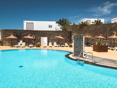 Large pool with sun umbrellas and lounge chairs under clear sky at a hotel.