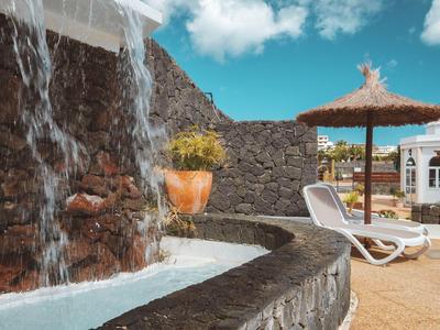 An outdoor pool area with a waterfall, lounge chairs, and umbrellas in front of a stone wall.
