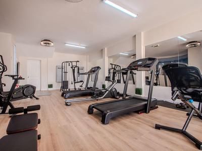 Modern fitness room with treadmills, exercise bikes, and other equipment on wooden floor.