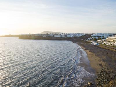 Linia brzegowa z piaszczystą plażą, falami i budynkami wzdłuż promenady o zachodzie słońca.
