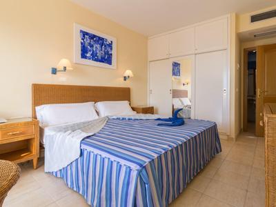 Jasno urządzone pokoje hotelowe z łóżkiem podwójnym, paskowanym narzutą i stolikami nocnymi.