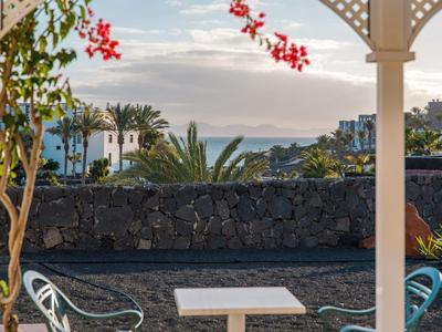 Taras z stołem i krzesłami z widokiem na morze i budynki o zachodzie słońca.