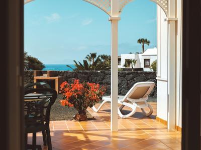 Výhled z interiéru na terasu s lehátkem, květinami a mořem v pozadí.