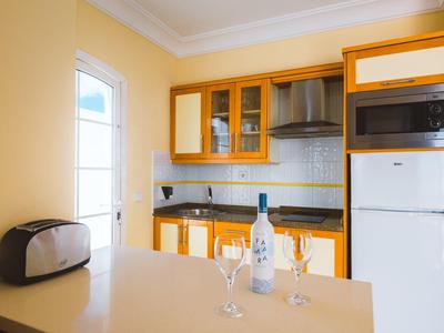 Nowoczesny aneks kuchenny z żółtymi szafkami, mikrofalówką, tosterem i butelką wina z kieliszkami.