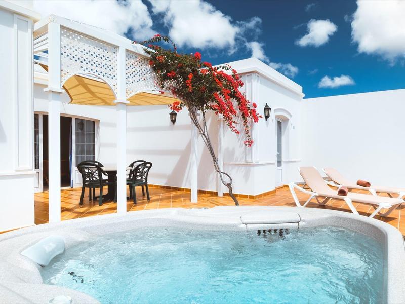 Jacuzzi na słonecznym tarasie obok białych budynków pod niebieskim niebem