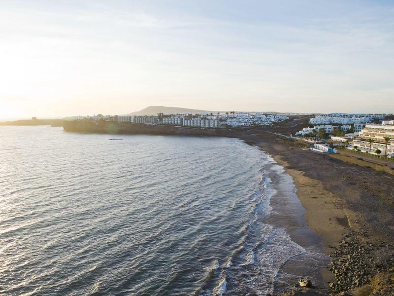 Linia brzegowa z piaszczystą plażą, falami i budynkami wzdłuż promenady o zachodzie słońca.