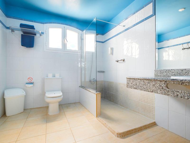 Jasna łazienka z niebieskimi ścianami, prysznicem bez brodzika i białymi urządzeniami sanitarnymi.