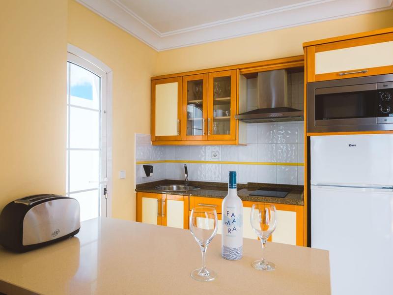 Nowoczesny aneks kuchenny z żółtymi szafkami, mikrofalówką, tosterem i butelką wina z kieliszkami.