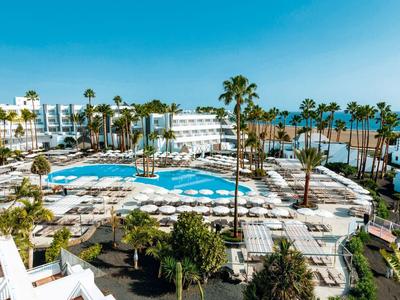 Grande piscina dell'hotel con lettini, palme, vista sul mare e cielo azzurro.