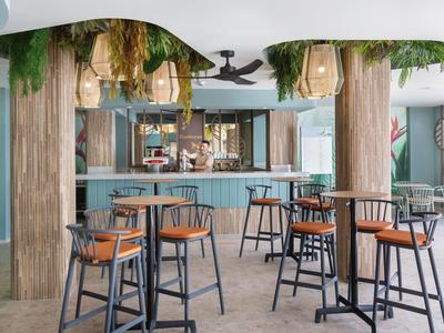 Area bar d'hotel moderna con sedute blu e decorazioni naturali di piante sospese.