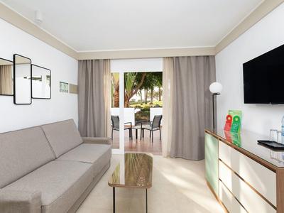 Camera d'hotel moderna con divano, TV e balcone con vista sulle palme.