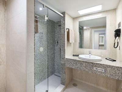 Bagno luminoso con doccia in vetro, grande specchio e lavandino su piano in marmo.