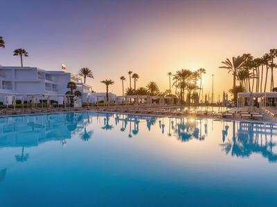 Zwembad bij zonsondergang met palmbomen en hotelgebouwen op de achtergrond