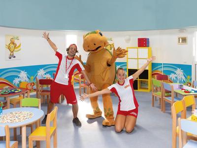 Angolo giochi colorato per bambini con due animatori e una mascotte in un hotel.