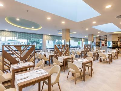 Ristorante moderno e luminoso con tavoli, sedie e divisori decorativi sotto una finestra zenitale.